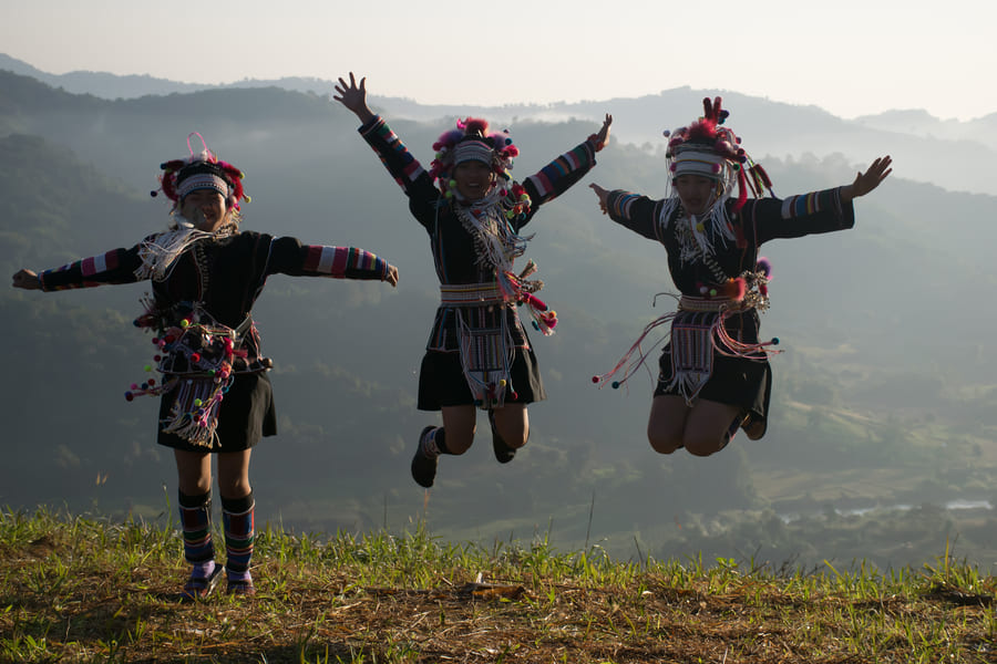 Imagen de 3 personas del grupo étnico Akha en China Saltando en una montaña